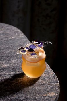 a small glass vase with flowers in it on top of a marble table next to a black wall