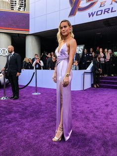 a woman in a purple dress standing on a purple carpet with people watching from the sidelines