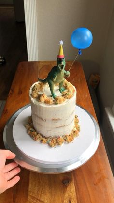 a birthday cake with a toy dinosaur on top and a balloon in the air above it