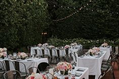 an outdoor dining area with tables and chairs set up for a formal dinner in the garden