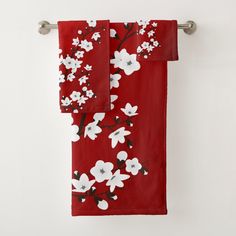 a red towel with white flowers on it hanging from a metal hook in front of a white wall