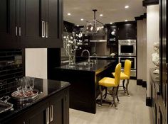 a kitchen with black cabinets and yellow chairs