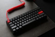 a computer keyboard and mouse on a desk with a red cord plugged in to it