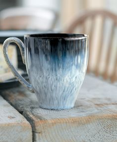 a blue and white coffee cup sitting on top of a wooden table next to a plate