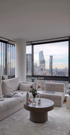 a living room filled with white furniture and tall buildings in the backgroung