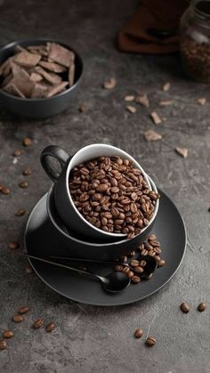 two cups filled with coffee beans sitting on top of a black saucer and plate