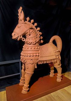 a wooden sculpture of a horse on display in a room with black walls and wood flooring