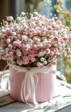 pink and white flowers in a pink box on a window sill with ribbon tied around it