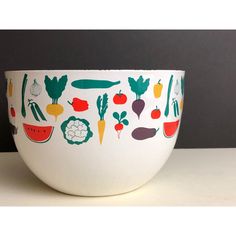 a white bowl with vegetables painted on the front and sides, sitting on a table