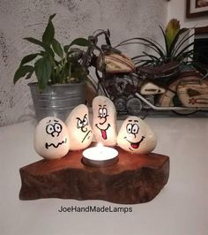 three eggs with faces on them sitting next to a lit candle in front of a potted plant