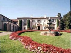 a large house surrounded by lush green grass and red flowers in the front yard area