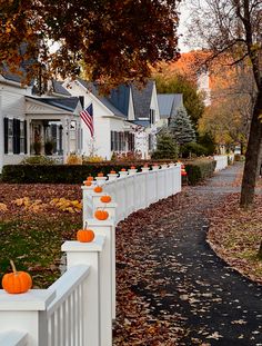 a white picket fence with pumpkins on it and some houses in the back ground