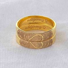 two gold wedding rings with engraved names on the sides and hearts in the middle, set against a white background