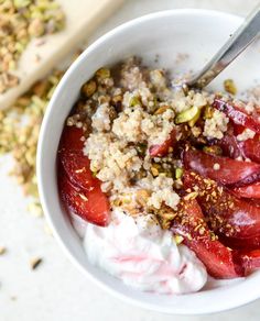 a bowl filled with strawberries and granola on top of a white table next to a spoon