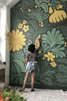 a woman painting a wall with yellow flowers on green and yellow florals in the background