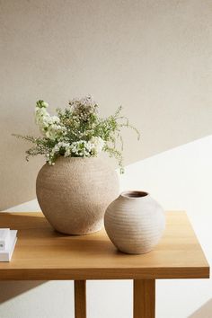 two vases sitting on top of a wooden table next to each other with flowers in them