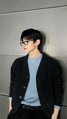 a young man wearing glasses leaning against a wall