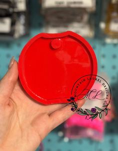 a hand holding a red plastic object in front of a shelf with other items on it