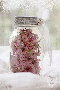 pink flowers are in a glass jar on a white tablecloth with an old - fashioned background