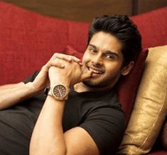 a man sitting on top of a red couch next to pillows and a clock in his hand