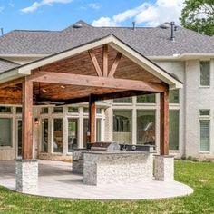 an outdoor kitchen and grill area in front of a large white brick house with wood beams on the roof