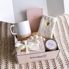 a pink box with some items in it sitting on a blanket next to a mug