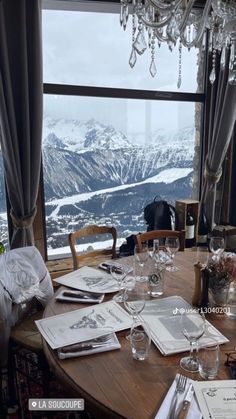 the table is set with wine glasses, silverware and napkins in front of a large window overlooking mountains