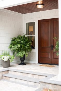 a house with two potted plants on the front steps and a wooden door in the background