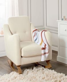 a white chair with a blanket on top of it next to a dresser and drawers