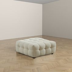 a white ottoman sitting on top of a hard wood floor in an empty room with parquet floors