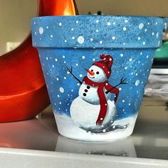 a pot with a snowman painted on it sitting on top of a counter next to a red object