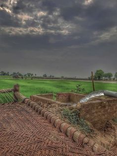 an old brick building sitting in the middle of a green field under a cloudy sky