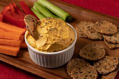 hummus and crackers on a wooden tray with carrots, celery, and pickles