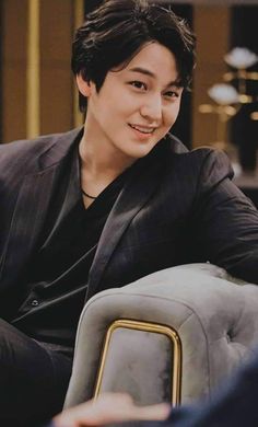 the young man is sitting down and smiling at the camera while wearing a black suit