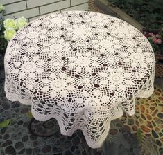 a white doily covered table sitting on top of a stone floor next to flowers