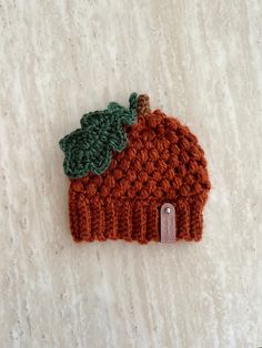 a crocheted hat with a green leaf on it sitting on a white surface