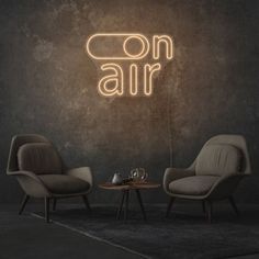 two chairs and a table in front of a neon sign that says on air above them