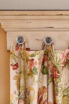 an open window with floral curtains hanging from it's rodulage and two knobs on each side