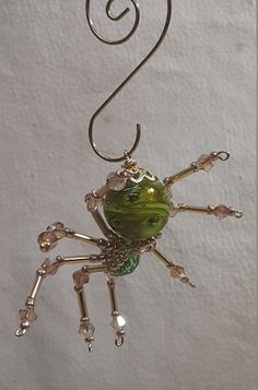 a green glass spider hanging from a hook on a white wall with a spiral wire attached to it's back