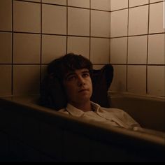 a man laying in a bathtub with his head resting on the back of it