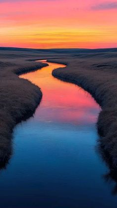 a river running through a lush green field under a colorful sky with clouds in the distance