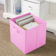 a pink storage bin with files and magazines in it next to a white bookcase