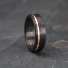 a black and gold wedding band with two stripes on the inside, sitting on top of a stone surface