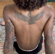 the back of a woman with tattoos on her upper and lower back, sitting on a bed