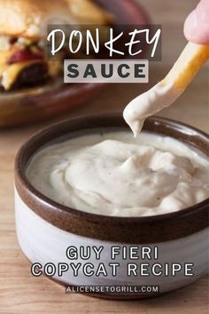 a person dipping some kind of sauce into a bowl with a sandwich in the background