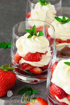 two desserts with strawberries and whipped cream in them on a wooden cutting board