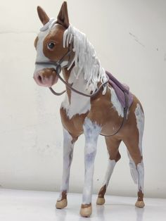 a toy horse with white and brown paint on it's face, standing in front of a white wall