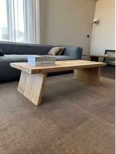 a wooden table sitting on top of a carpeted floor next to a gray couch