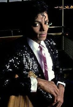 a man in a sequin jacket and tie posing for the camera with his arms crossed