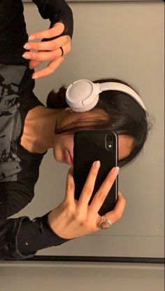 a woman with headphones on taking a selfie in front of her cell phone